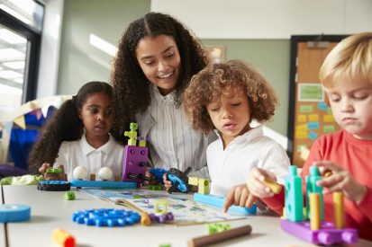 female-teacher-sitting-at-table-in-play-room-with-three-kindergartne-children-constructing.jpg